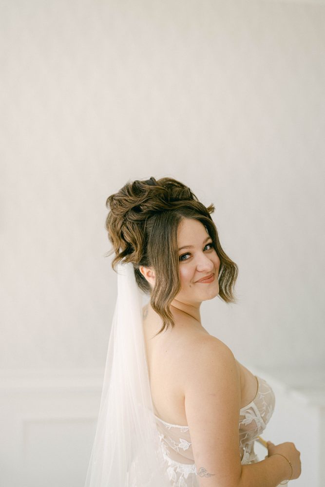 nj_hair_glam_updo_Stella_Fatale Bride looking to side, has updo with face framing pieces from bridal hair company Stella Fatale and lace wedding dress