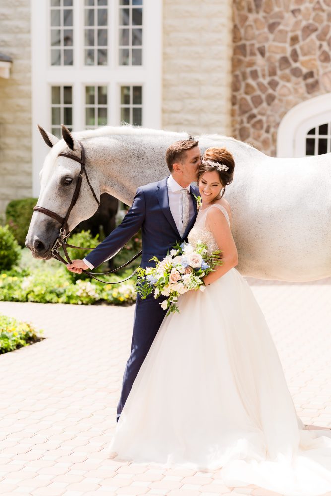 new-jersey-wedding-bride-groom-elegant-venue.jpg Romantic New Jersey bride with textured updo and pearl hair accessory holding bouquet beside groom and horse