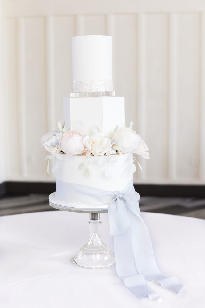 elegant-new-jersey-wedding-cake-ballroom-reception.jpg Minimalist white wedding cake with soft blue ribbon and floral accents styled for formal ballroom reception